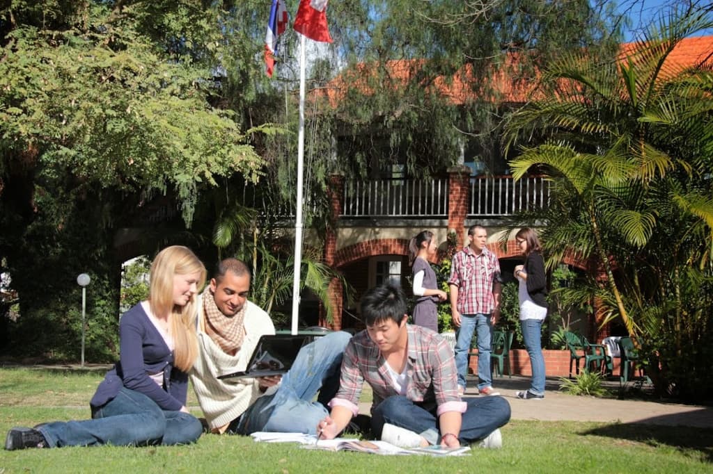 フェニックスアカデミーのキャンパスの芝生に座って勉強する学生たち