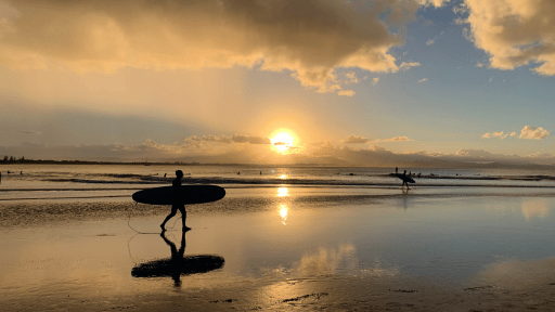 朝日が昇る海辺でサーフィンをする人たち